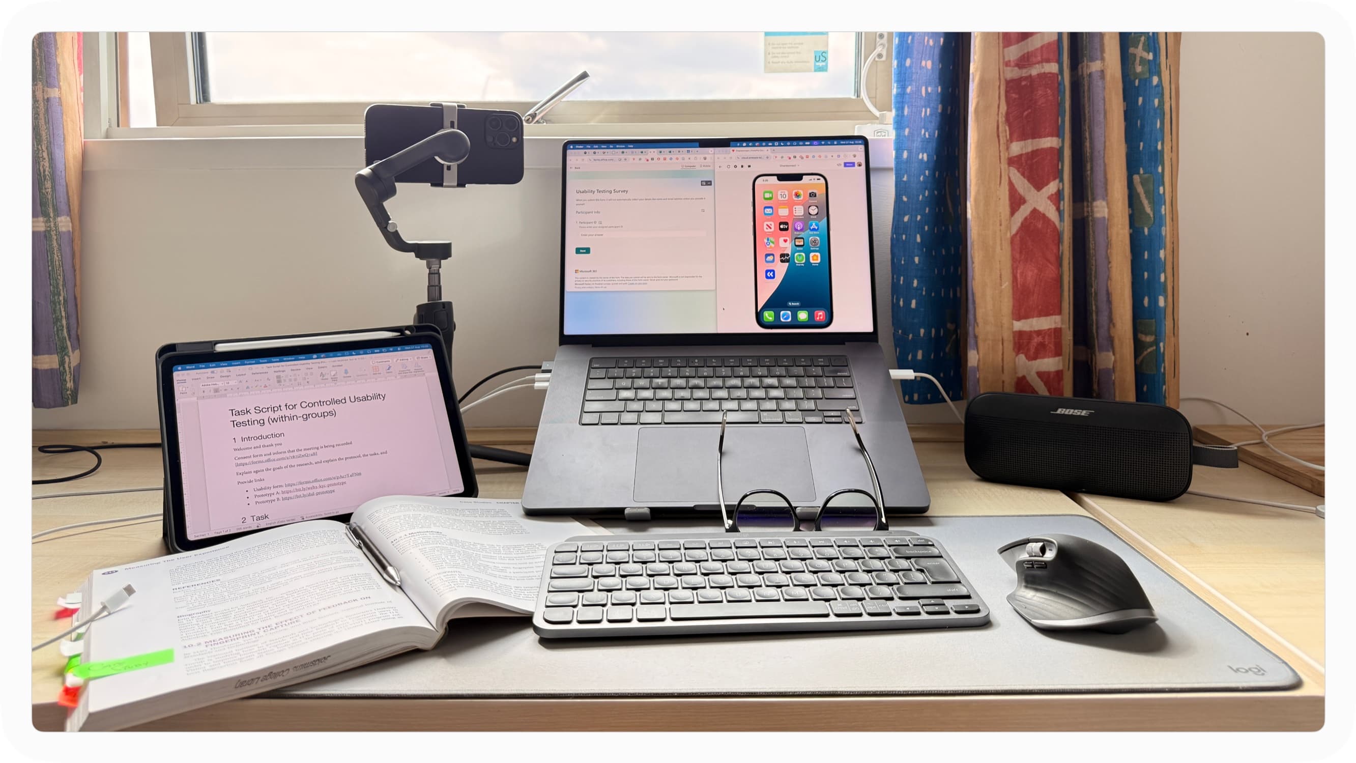 Desk setup for moderated remote testing: laptop with prototype and video call, notebook and phone rig